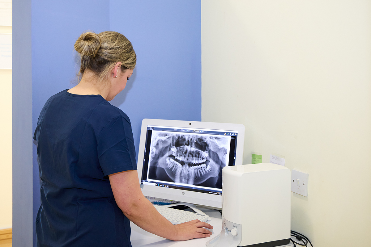 picture of a Female orthodontist in navy scrubs examining a panoramic orthodontic X-ray on a computer screen in a clinical setting