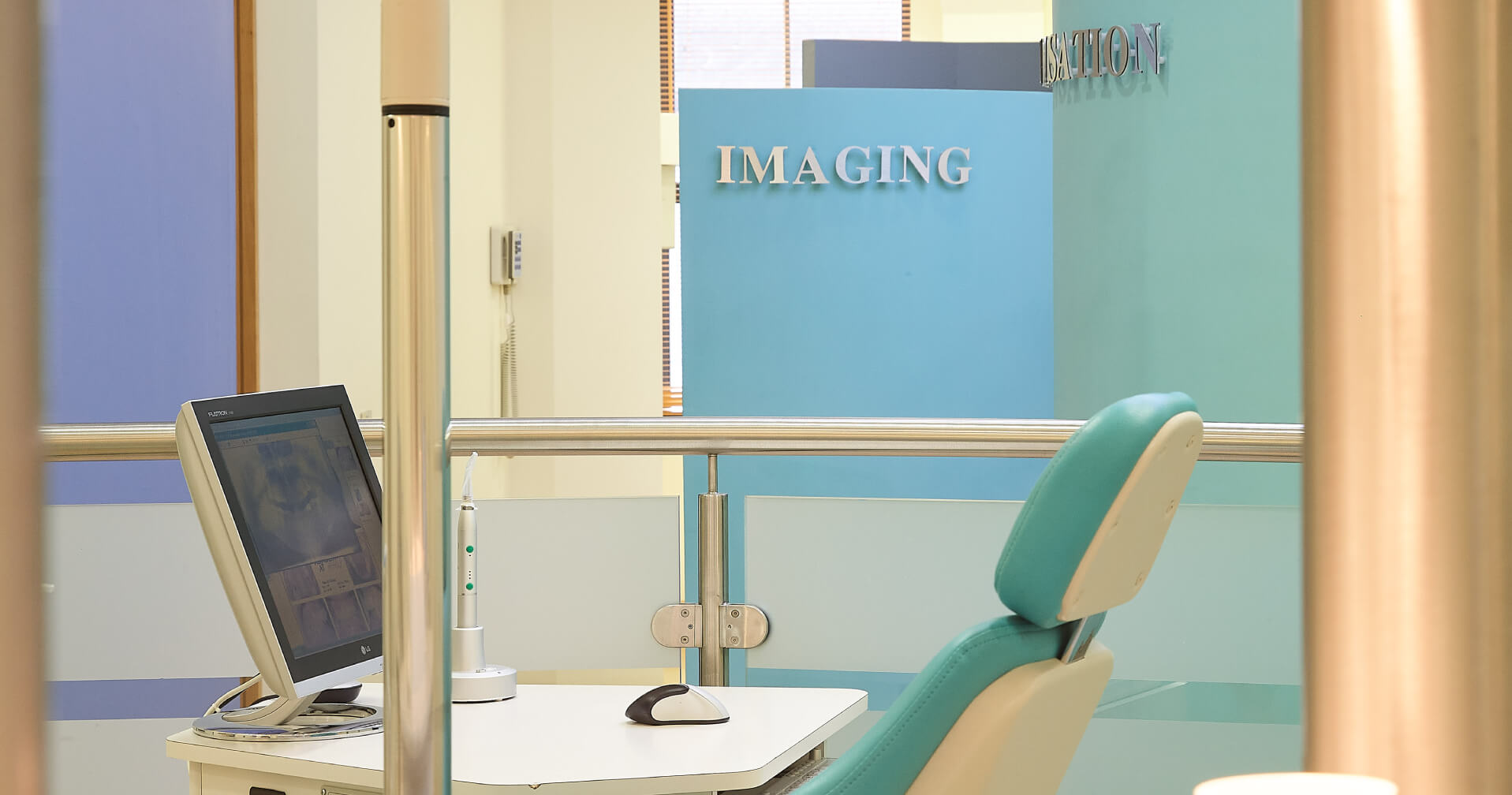 picture of a Modern orthopedic imaging room with a teal patient chair, computer monitor displaying medical scans, and a blue sign reading 'IMAGING' in the background