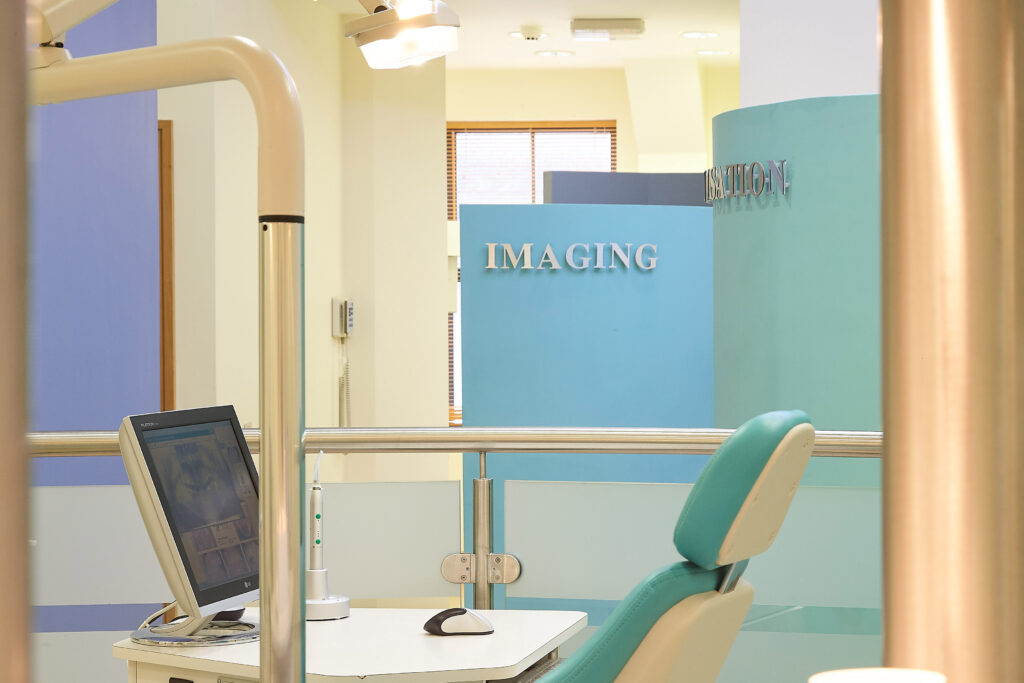 Orthodontic imaging room with modern dental chair in teal, computer monitor displaying dental scan, and blue wall featuring signage saying "IMAGING"