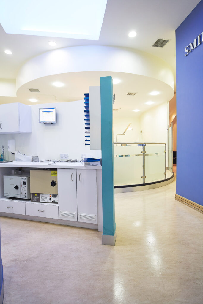 A bright dental office waiting area with white cabinets, a light blue wall, and a curved glass partition in the background