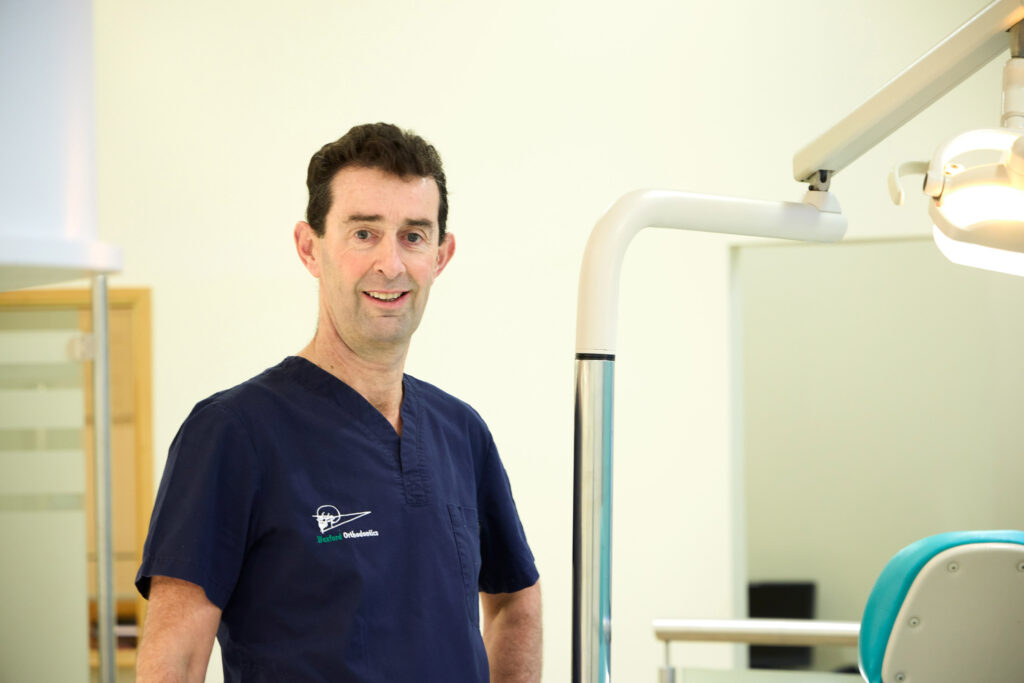 Picture of an Orthodontist in navy scrubs standing beside a bright orthodontic light