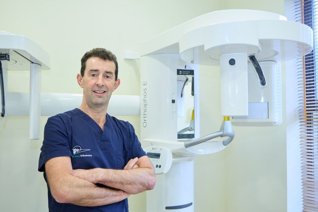 Picture of an Orthodontist in navy scrubs standing beside an orthodontic x-ray