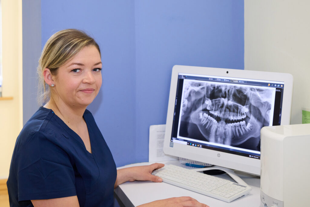 Picture of an orthodontic assistant in navy scrubs viewing an x-ray of a jaw facing the camera