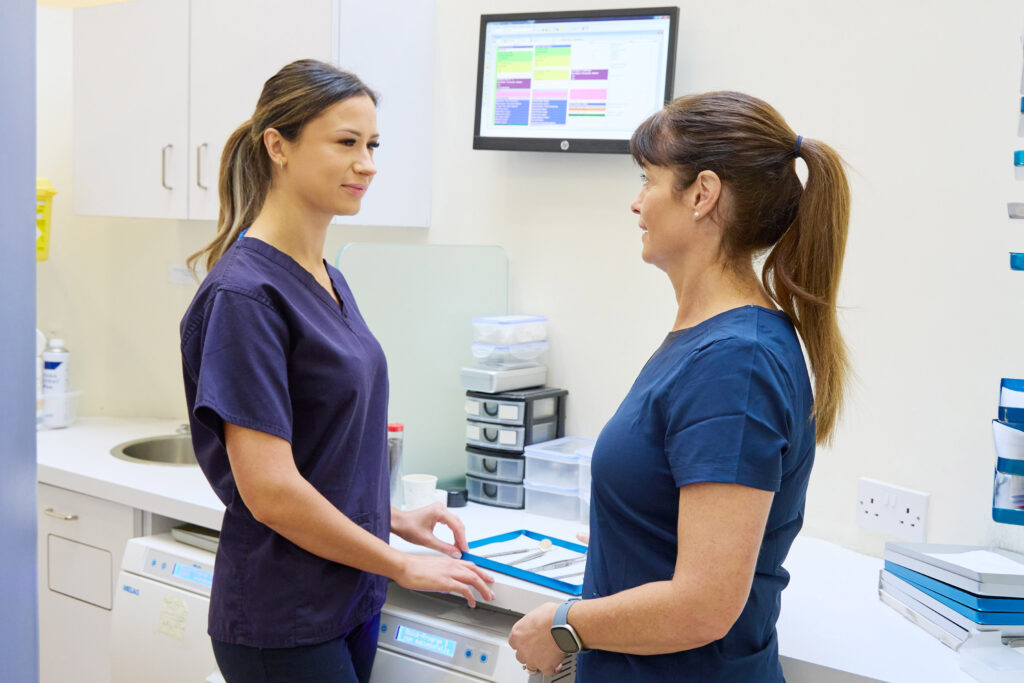 picture of two orthodontists in navy scrubs talking in a room with a computer on the wall and orthodontist tools on counter top